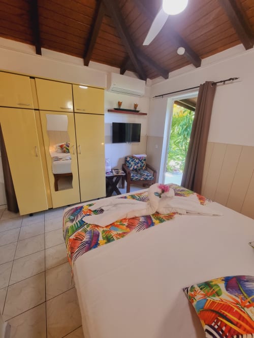Colorful studio bedroom at Gites Kaladja with double bed, yellow wardrobe, TV, and garden view access in Port-Louis