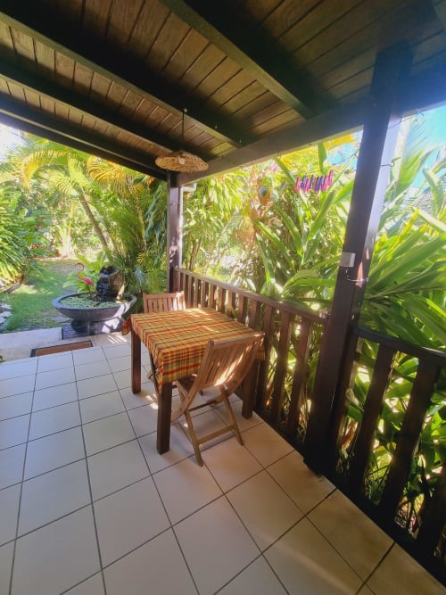 Covered patio with wooden table and chairs overlooking lush tropical garden at Gites Kaladja studio in Guadeloupe