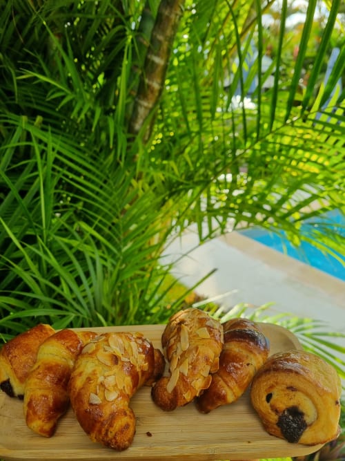Fresh pastries and croissants at Gites Kaladja breakfast with tropical palm fronds backdrop in Port-Louis