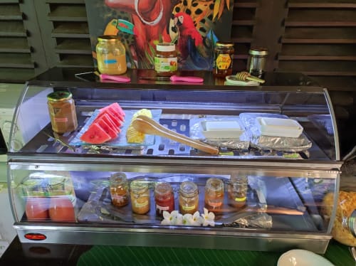 Breakfast display case at Gites Kaladja BnB in Port-Louis showing fresh fruits, jams, honey, and pastries