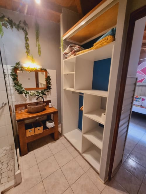 Modern bathroom with wooden vanity, green plant wreath, and white storage shelves at Gites Kaladja apartment in Guadeloupe