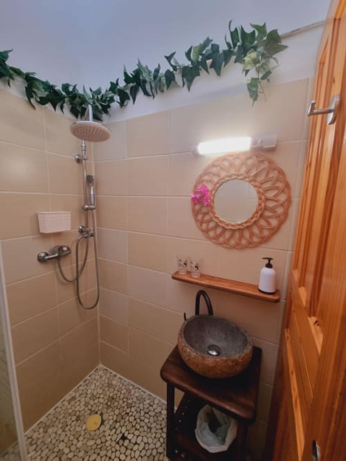 Modern shower room at Gites Kaladja in Port-Louis with rainfall showerhead, decorative woven mirror, natural stone sink, and