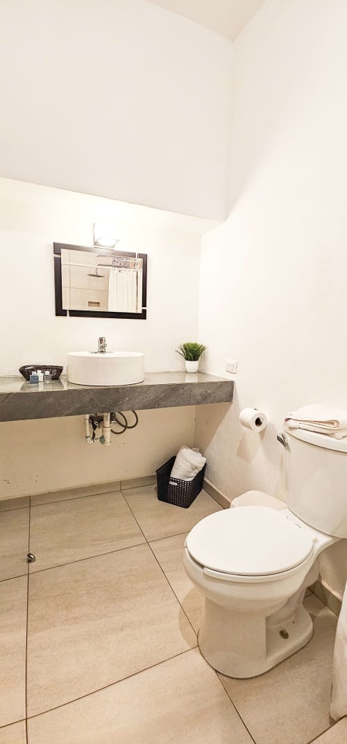 Modern bathroom in La Familia Hotel Queen Room, San Blas with white toilet, sink, dark countertop and tiled floor.