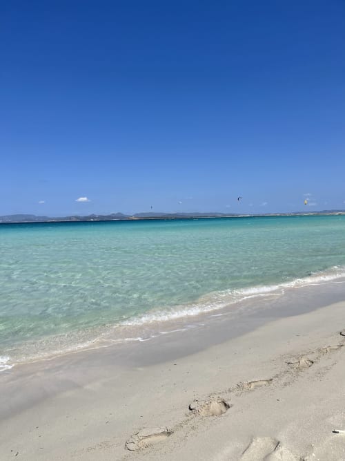 Aguas turquesas y playa arenosa en Formentera Especial, La Savina con kitesurfistas y cielo azul despejado