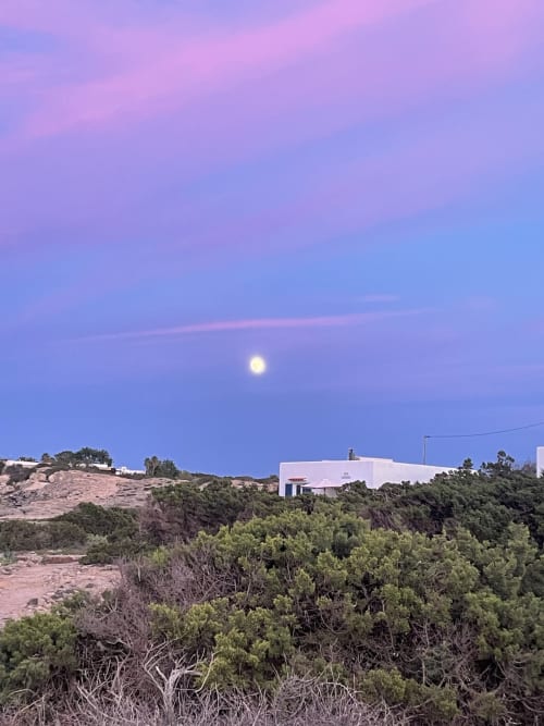 Luna llena brillando sobre paisaje mediterráneo con villa moderna blanca entre pinos, Formentera
