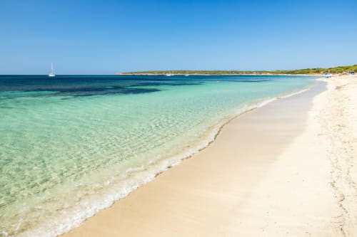 Playa virgen de aguas turquesas en Formentera con arena blanca, aguas cristalinas y velero frente a la costa de La Savina