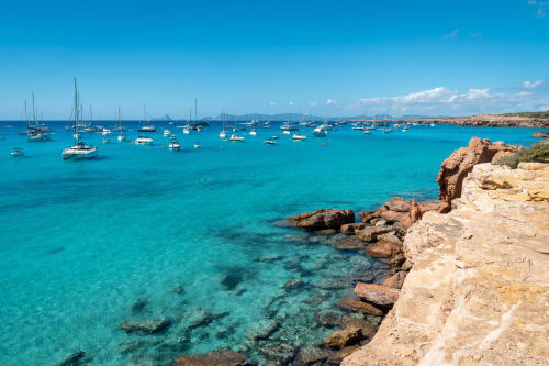Bahía de aguas cristalinas turquesas con veleros fondeados y acantilados rocosos en Formentera, La Savina