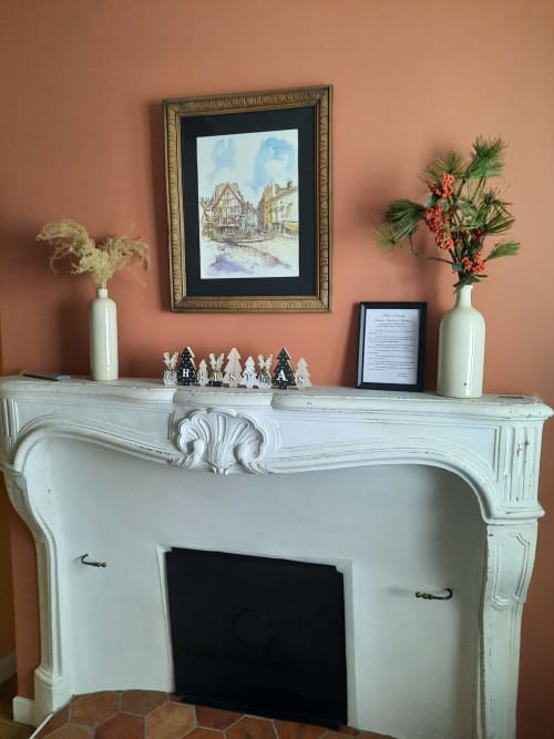 Manteau de cheminée élégant à la Maison Rinette Dijon avec finition blanc peint, objets décoratifs et œuvres encadrées sur fond corail