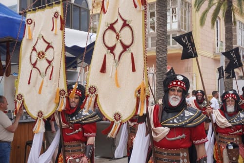Procesión en Carboneras con ornados estandartes religiosos y participantes disfrazados cerca del Hostal Juan Carlos