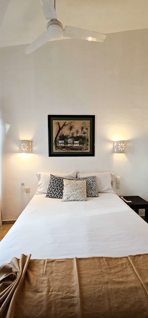 Queen bedroom at La Familia Hotel in San Blas with white bed, patterned pillows, framed art, and decorative wall sconces