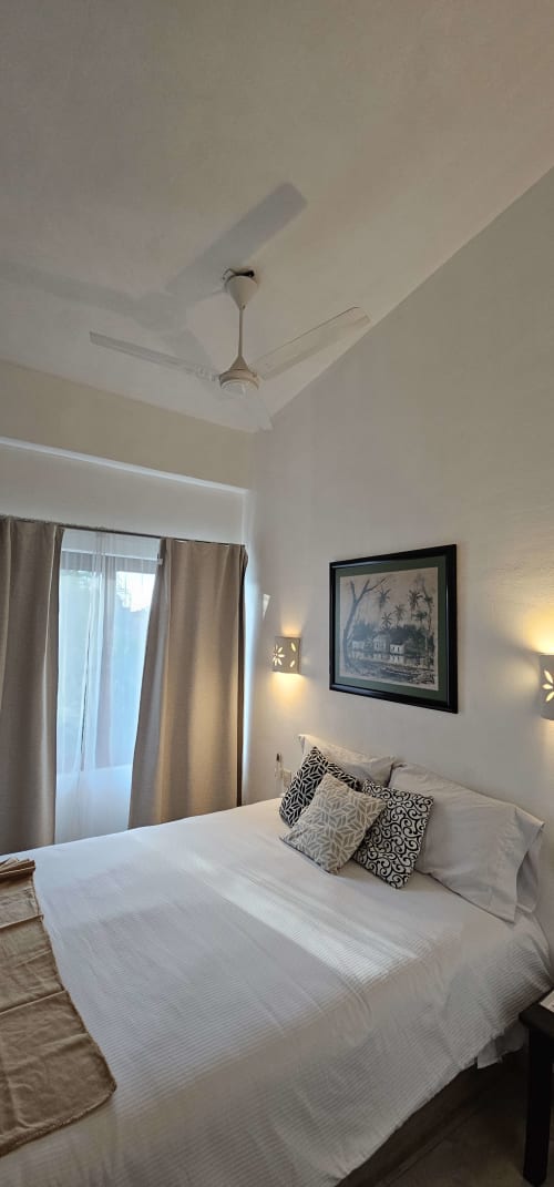 Clean queen bedroom at La Familia Hotel in San Blas with ceiling fan, framed artwork, and ocean view curtains