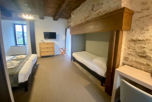 Chambre de l'Hôtel Saint Roch à Saint Ybard avec lits jumeaux, lit superposé, poutres en bois et murs en pierre