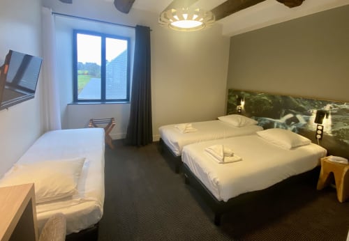 Chambre de l'hôtel Saint Roch à Saint Ybard avec deux lits, éclairage moderne, fenêtre sur paysage champêtre et décor contemporain