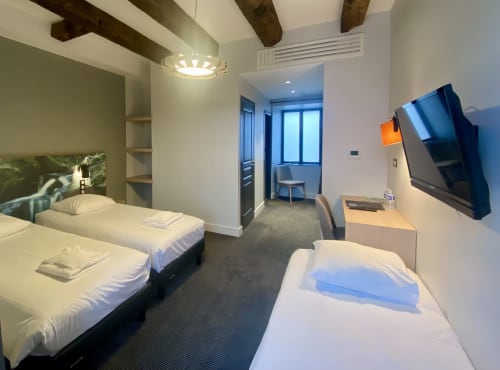 Chambre triple moderne à l'Hôtel Saint Roch à Saint Ybard avec lits jumeaux, télévision et poutres apparentes