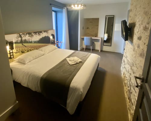 Chambre moderne à l'Hôtel Saint Roch à Saint Yrieix avec lit queen-size, mur en pierre et mobilier contemporain.