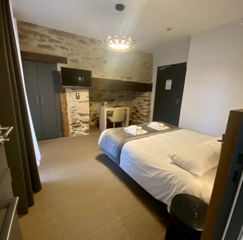 Chambre moderne de l'Hôtel Saint Roch avec lit, bureau et salle de bain attenante aux murs en pierre