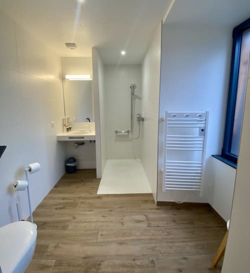 Salle de bains moderne à l'Hôtel Saint Roch avec douche à l'italienne, lavabo, toilettes, sèche-serviettes chauffant et sol imitation bois