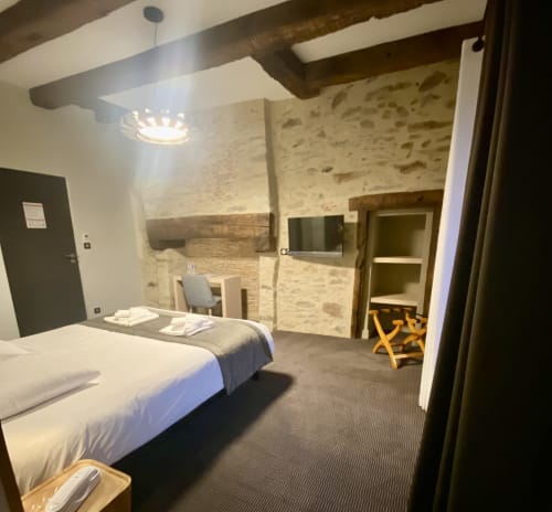 Chambre d'hôtel moderne à l'Hôtel Saint Roch avec murs en pierre apparente, poutres en bois et mobilier contemporain à Saint Ybarld