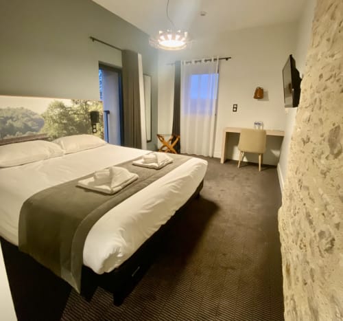 Chambre d'hôtel moderne à l'Hôtel Saint Roch à Saint Yrieix avec lits jumeaux, mur en pierre et mobilier contemporain