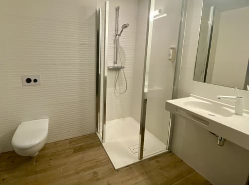 Salle de bains moderne de l'Hôtel Saint Roch avec douche à l'italienne, sanitaires blancs et parquet