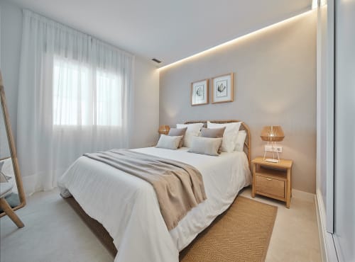 Dormitorio moderno con cama de madera, sábanas blancas, toques beige, cortinas translúcidas e iluminación cálida en Puerto Santa María