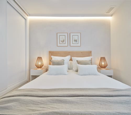 Dormitorio moderno con cabecero de madera, ropa de cama blanca, lámparas de latón y arte botánico en el apartamento Wehost Costaluz