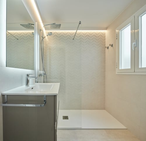 Baño moderno con ducha de azulejos espiga, vanidor blanco y mampara de vidrio en apartamento Wehost Costaluz en Puerto