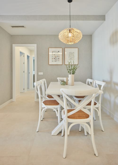Comedor moderno con sillas blancas, mesa redonda, lámpara colgante tejida y decoración costera en apartamento de Puerto Santa María.