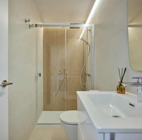 Baño moderno en apartamento Wehost Costaluz con ducha, lavabo blanco, inodoro y azulejos neutros en Puerto