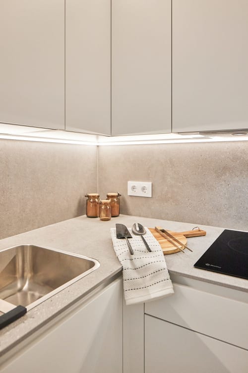 Encimera de cocina moderna con fregadero de acero inoxidable, mostradores blancos, utensilios de cocina y tablas de cortar de madera en Wehost