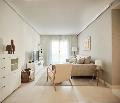 Sala de estar moderna con sofá beige, silla de madera, almacenaje blanco y luz natural desde el balcón en Wehost Costaluz