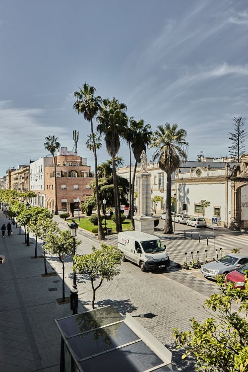 Vista de la plaza Puerto Santa María desde el balcón con palmeras, edificios históricos y vehículos estacionados bajo cielo azul