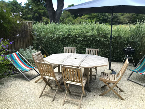 Terrasse du cottage Moulin d'Angibaud avec table à manger en bois, chaises, parasols et transats entourés de haies