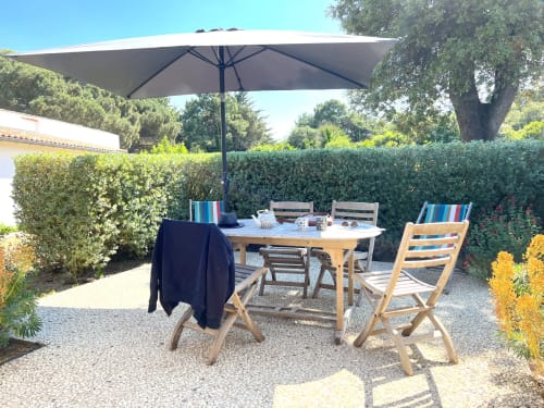 Terrasse du gîte Moulin d'Angibaud avec chaises en bois, table et coussins rayés sous un grand parasol noir à La