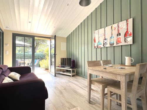 Séjour du gîte Vert avec mur d'accent vert, table à manger en bois, canapé violet et vue sur le jardin