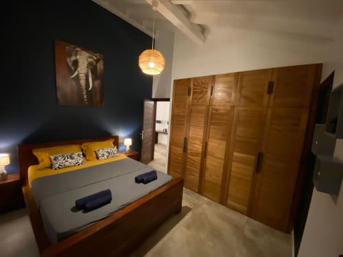 Chambre de la villa Passion Vanille aux Hébergements Passion avec lit en bois, coussins jaunes, armoire et luminaires suspendus