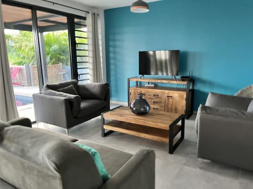 Séjour moderne aux murs turquoise, téléviseur écran plat, mobilier bois, sièges gris et vue sur mer à Passion