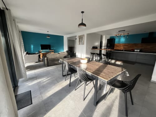 Villa contemporaine avec cuisine et salle à manger ouvertes, mur accent bleu-vert, table en bois, chaises noires et vue sur mer