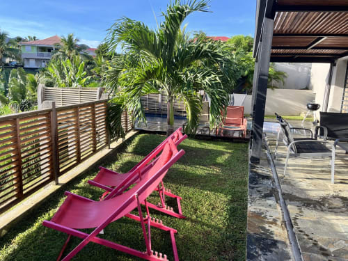 Chaises longues roses dans un jardin tropical avec palmiers, clôture en bois et terrasse aux Hébergements
