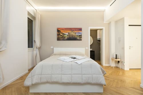 Modernes Schlafzimmer in den Magnolia Apartments Mailand mit weißem Bett, Holzböden und Kunstwerk der Mailänder Kathedrale