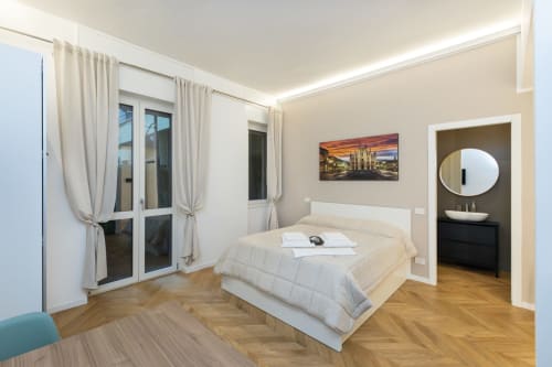Modernes Schlafzimmer in den Magnolia Apartments Mailand mit weißem Bett, Parkettboden, Balkontüren und rundem Ensuite-Bad