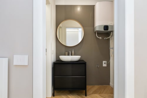 Modernes Badezimmer in Mailänder Apartment mit rundem Spiegel, weißem Aufsatzwaschbecken, schwarzem Waschtisch, taupefarbenen Wänden und Holzboden