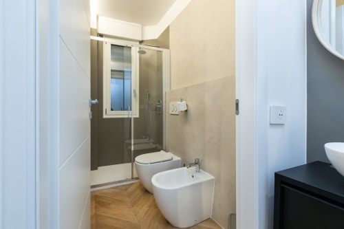 Modernes Badezimmer in den Magnolia Apartments Mailand mit weißem Bidet und Toilette, gläserner Duschkabine und Holzboden