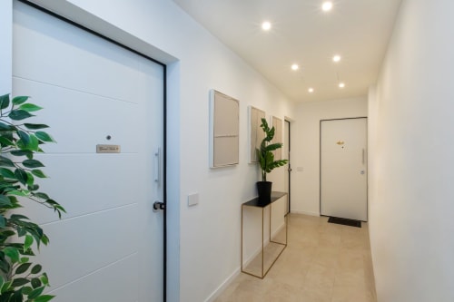 Moderner Flur in Mailänder Wohnung mit weißen Türen, Einbauleuchten, Topfpflanze und neutralem Bodenbelag