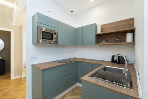 Moderne türkisfarbene Küche mit Holzarbeitsplatte, Mikrowelle, Spüle und offenen Regalen in den Magnolia Apartments Mailand
