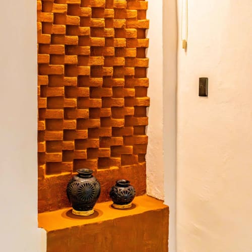 Nicho de Casa Sofi Oaxaca con muros de ladrillo terracota y vasijas cerámicas negras en repisa naranja