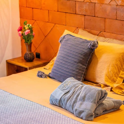 Dormitorio colorido en Casa Sofi Oaxaca con ropa de cama amarilla, almohada azul, toallas dobladas y flores rosas en la mesita de noche