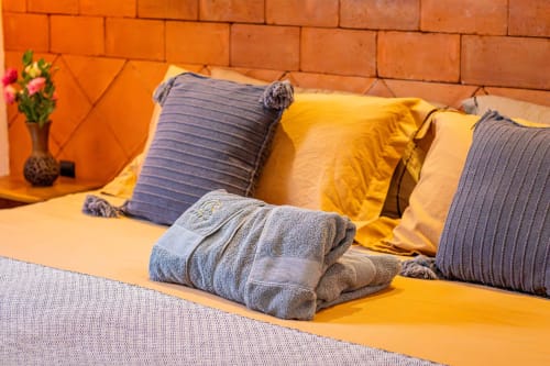 Habitación colorida en Casa Sofi Oaxaca con ropa de cama amarilla, almohadas a rayas grises y toallas dobladas contra una pared naranja vibrante