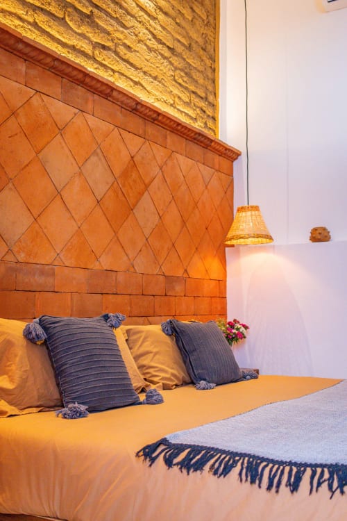 Acogedora habitación en Casa Sofi Oaxaca con pared de azulejos de barro, ropa de cama dorada y almohadas con rayas azules