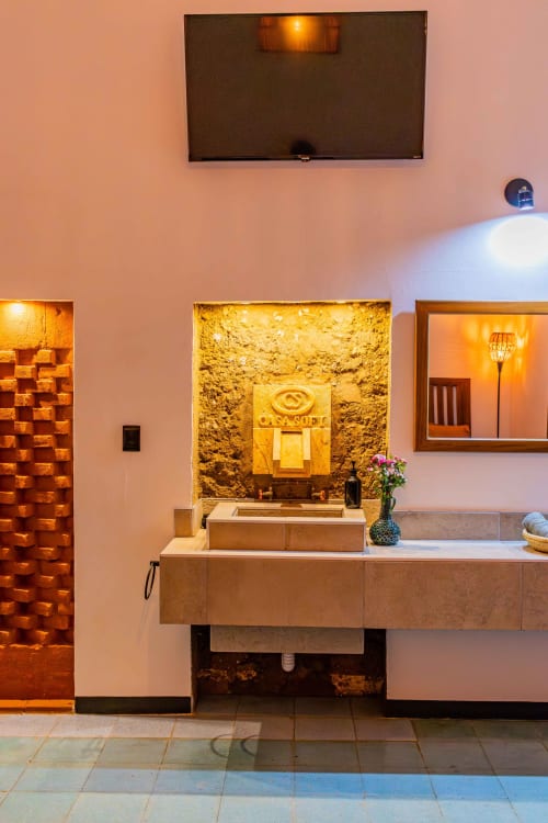 Lobby del hotel Casa Sofi Oaxaca con pared de piedra iluminada, lavabo y espejo bajo iluminación cálida